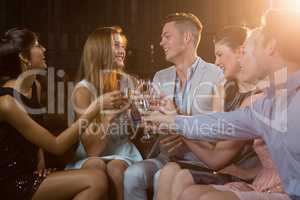 Group of smiling friends sitting on sofa and toasting a glasses of champagne