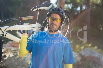 Portrait of male mountain biker carrying bicycle in the forest