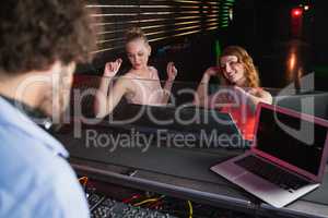 Male disc jockey playing music with two women dancing on the dance floor