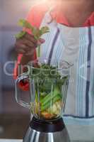 Mid-section of woman putting vegetable in a mixer