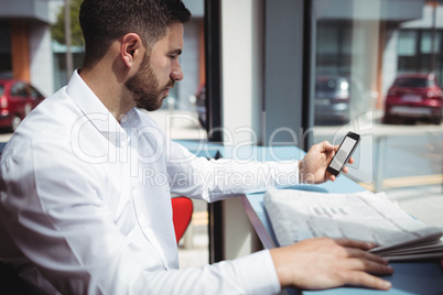 Man using mobile phone while reading newspaper