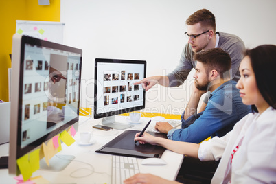 Executive using graphics tablet while colleagues discussing at creative office