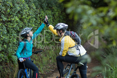 Biker couple giving high five while riding bicycle in countryside