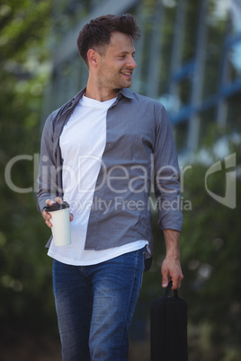 Handsome business executive holding disposable cup and bag