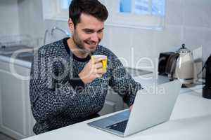 Man holding coffee mug while using laptop in the kitchen