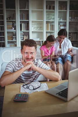 Smiling man sitting at table with bills and laptop