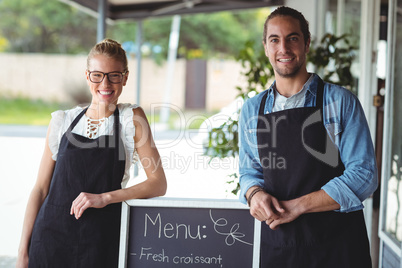 Waiter and waitress standing with menu board outside the cafe