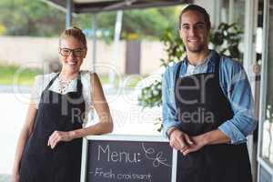 Waiter and waitress standing with menu board outside the cafe