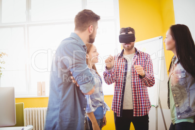 Coworkers looking at businessman wearing virtual reality headset