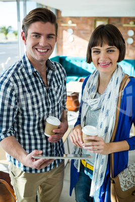 Portrait of smiling couple with coffee cups using a digital tablet