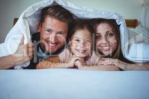 Happy family lying under a blanket on bed