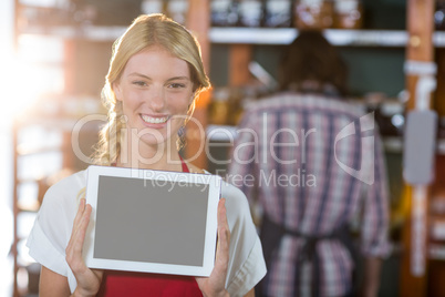 Smiling female staff showing digital tablet in supermarket