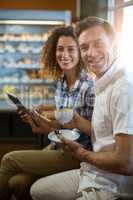 Man having cup of tea and woman using digital tablet in supermarket