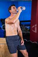 Shirtless athlete drinking water in gym