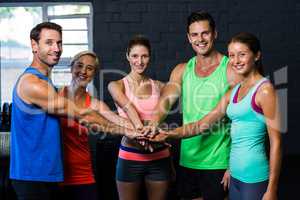Portrait of cheerful friends putting hands together in gym