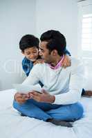 Father showing digital tablet to son on the bed