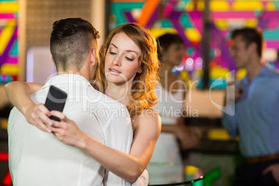 Woman checking her mobile phone while embracing a man