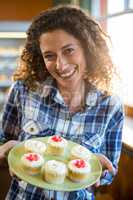 Smiling woman holding plate of cup cake in supermarket