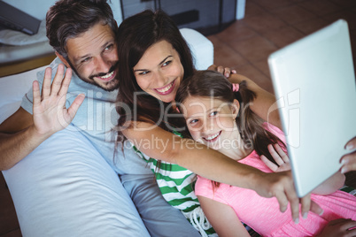 Parents sitting on sofa with daughter and clicking a selfie on digital tablet