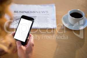 Woman using her mobile phone with newspaper and coffee cup on table