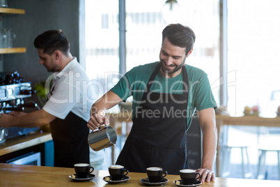 Smiling waiter making cup of coffee at counter