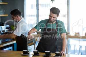 Smiling waiter making cup of coffee at counter