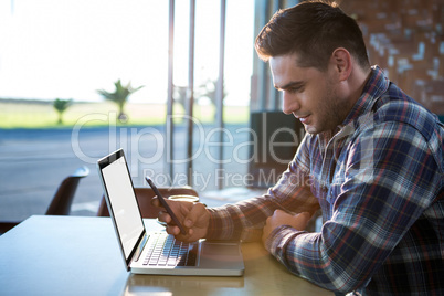 Man using mobile phone with laptop on table