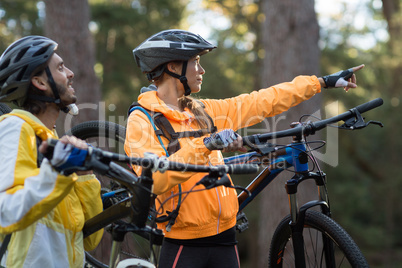 Biker couple carrying mountain bike and pointing in distance