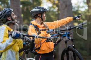 Biker couple carrying mountain bike and pointing in distance