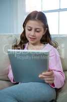 Girl using digital tablet while relaxing on sofa