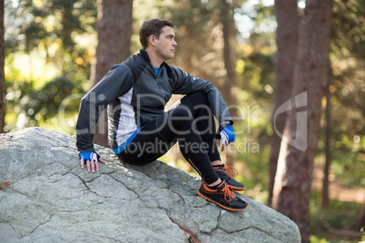 Male biker relaxing on rock in forest