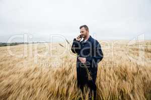 Farmer examining crops while talking on mobile phone in the field