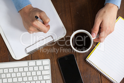 Man writing on clipboard while having cup of coffee