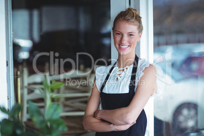 Portrait of smiling waitress standing with arms crossed