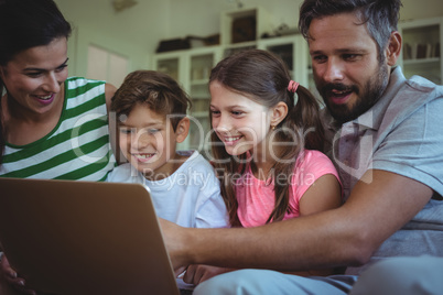 Parents sitting on sofa with their children and using laptop in living room