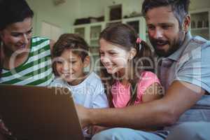 Parents sitting on sofa with their children and using laptop in living room