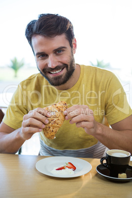 Smiling man having croissant in coffee shop