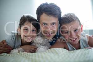 Portrait of father lying with their kids in bedroom