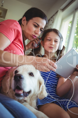 Mother and daughter sitting with pet dog and using digital