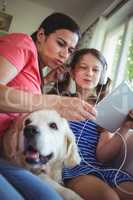 Mother and daughter sitting with pet dog and using digital