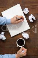Man crumpling paper while writing on notepad