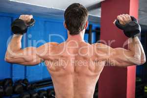 Rear view of shirtless athlete lifting kettlebells