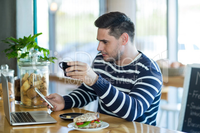 Man using a mobile phone while having cup of coffee