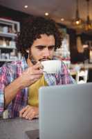 Man having coffee while looking at laptop