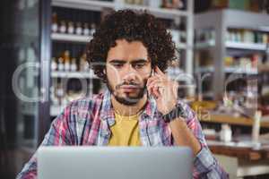 Man using laptop while talking on mobile phone