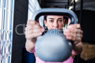 Serious female athlete lifting kettlebell in gym