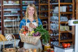 Smiling female staff holding basket of vegetables in organic section