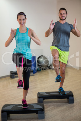 Smiling man and woman doing step aerobic exercise on stepper