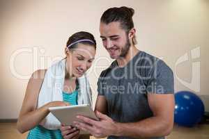 Smiling fitness trainer and woman using digital tablet