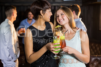 Female friends holding glass of cocktail in bar